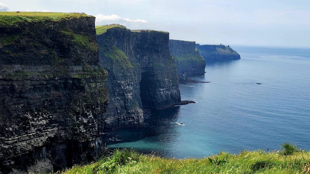 The mighty Cliffs of Moher at the sea's edge have black, limestone facings with the tops covered in bright green grass. 