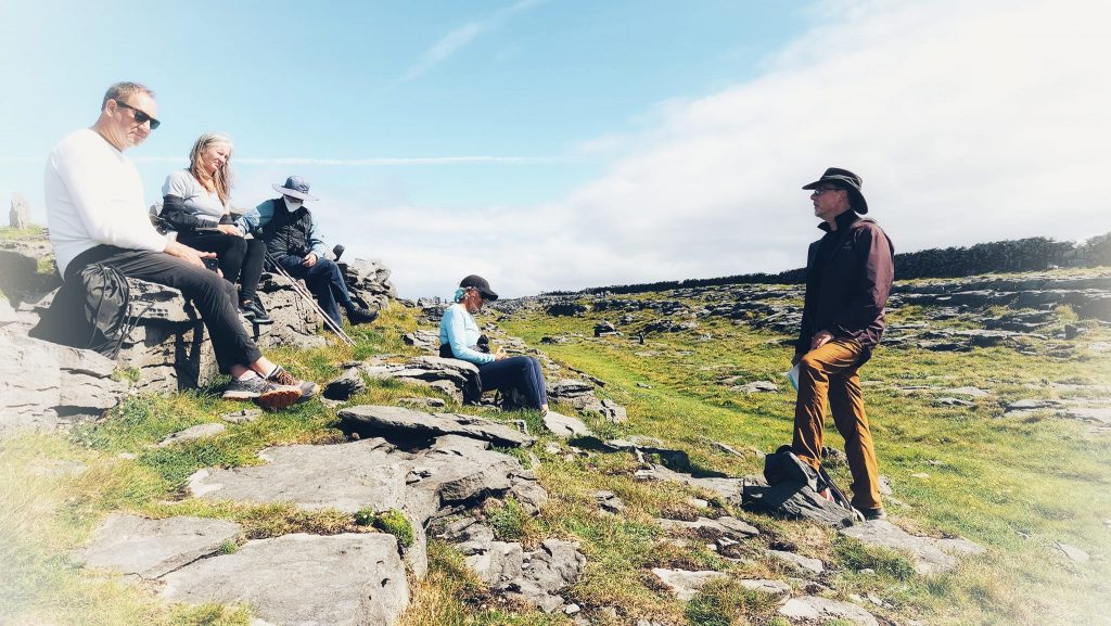 Modern day pilgrims use limestone rocks as seats while listening to their guide talk about the ancient history of the place. Pilgrimage to Ireland.