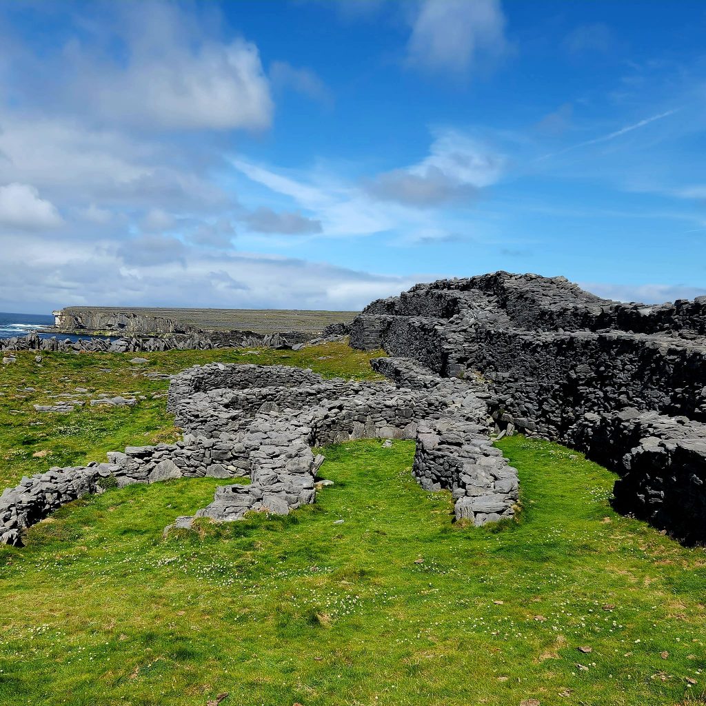 A large green field near ocean cliffs where the ancient ruins of The Black Fort stand - walls and fences made entirely of limestone. 