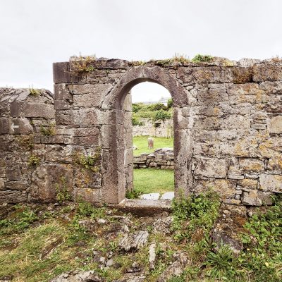 Ancient church ruins show the wall of an ancient church at a sight called The Seven Churches. There is an arched door opening. Through the opening is a small graveyard. The roofs are long gone, so the feeling is spacious. Pilgrimage to Ireland.