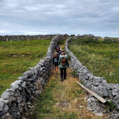 Modern day pilgrims hiking up grassy hill between two stone fences on pilgrimage to Ireland.