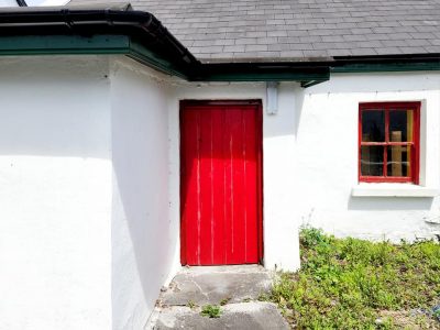 Charming white Irish cottage with bright red door and a window sill painted bright red.